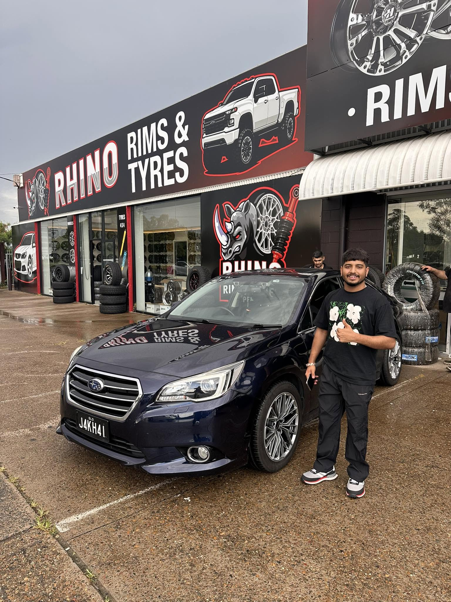 A blue Subaru sedan and a person outside Rhino Rims and Tyres
