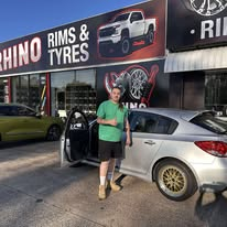 A silver sedan with gold wheels and a person outside the Rhino workshop