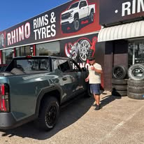 A grey ute with dark wheels and a person beside it outside Rhino