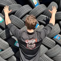 A person wearing a Rhino shirt in front of stacked tyres