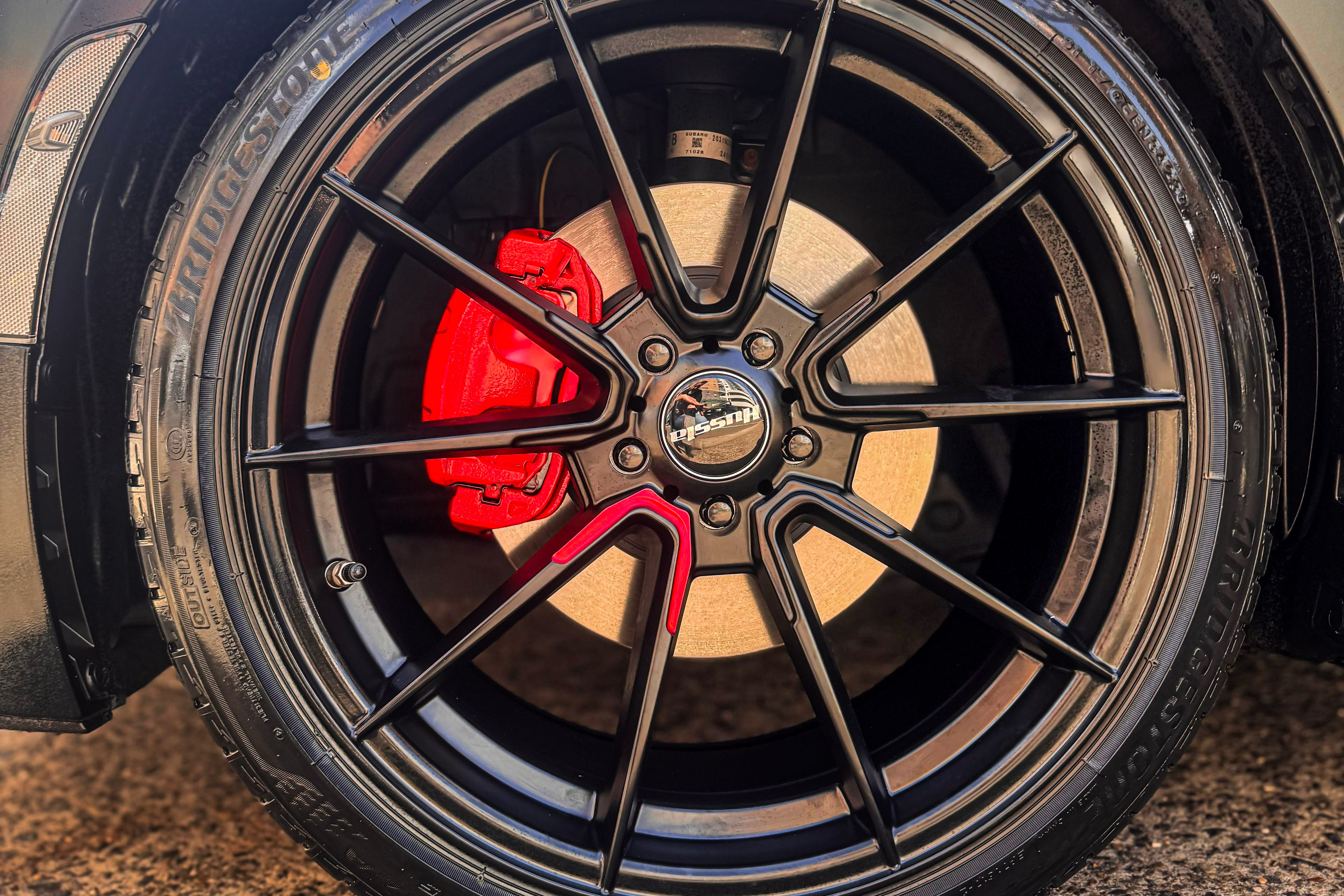 A black multi-spoke Hussla wheel with a red spoke accent and red brake calliper