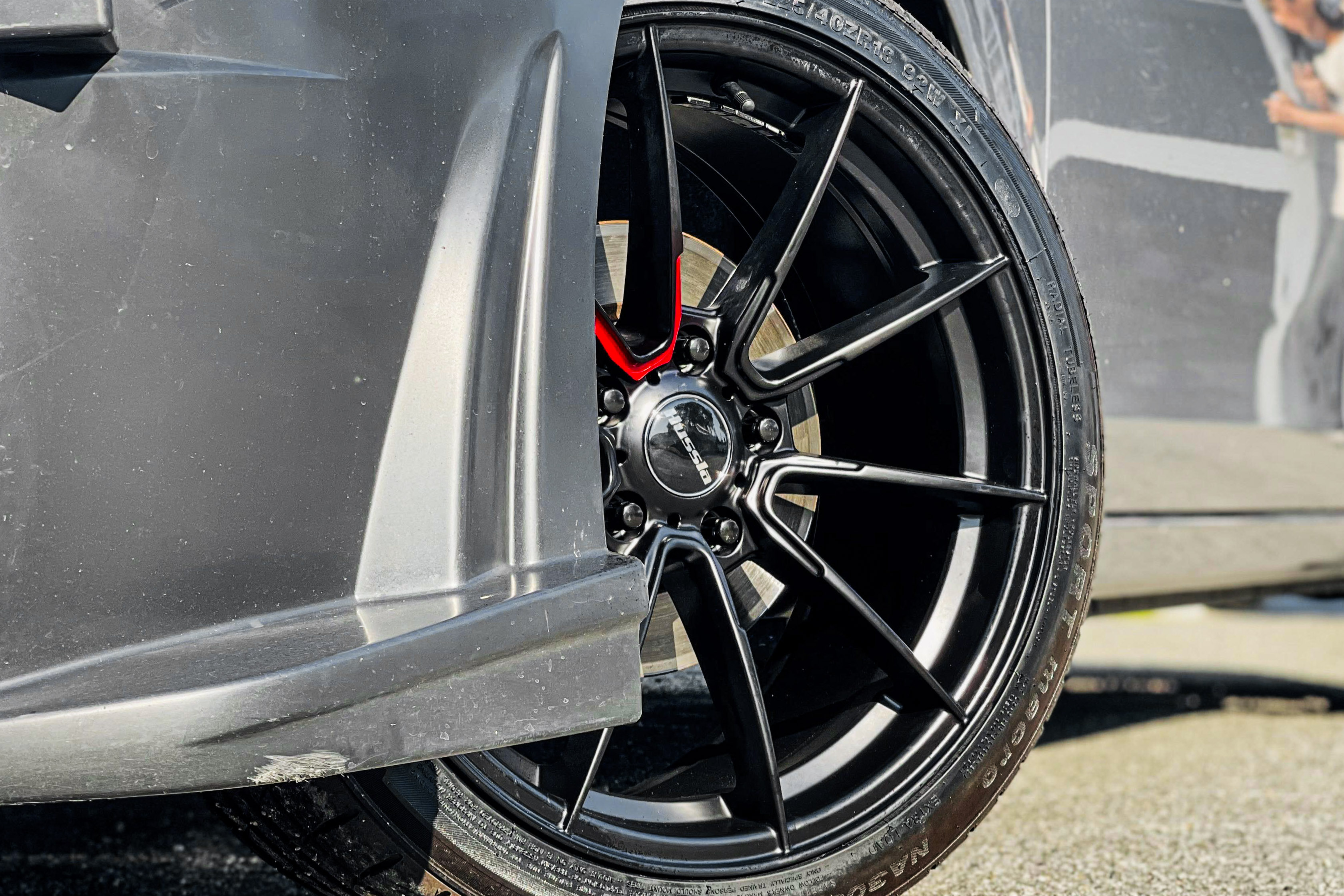 A black multi-spoke Hussla wheel with a red accent fitted to a silver Mitsubishi Lancer