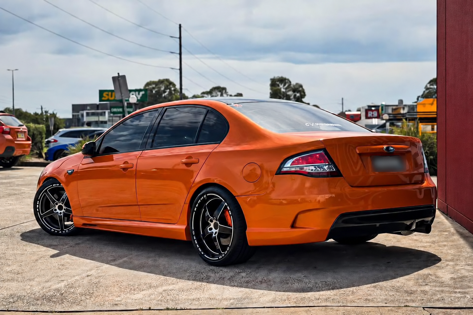 Orange sedan with black alloy wheels beside a plain maroon workshop wall